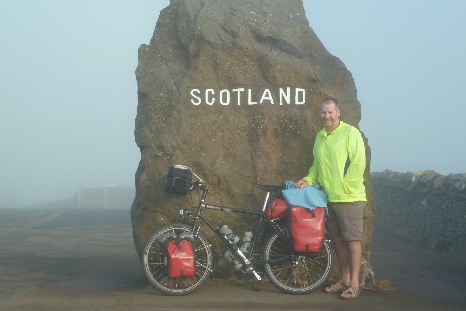 A person standing with a bike next to a large rock